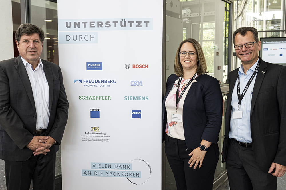 Three people pose next to a sign with a donor list.