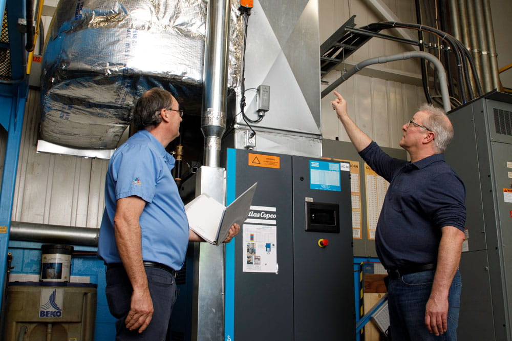 Two men are looking at an air compressor system.