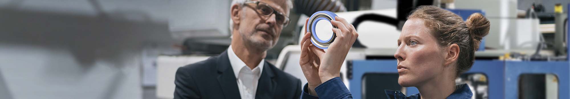 Man and woman standing in front of a turning machine looking at a blue seal together