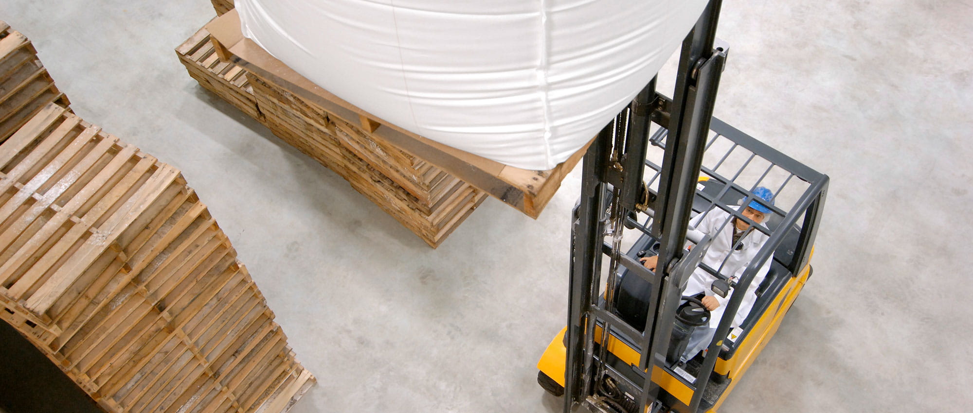Fork truck transports a large bag with materials and next to it are plates with wood