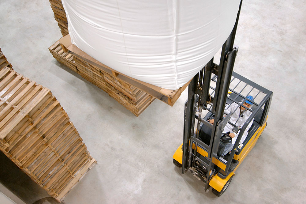 Fork truck transports a large bag with materials and next to it are plates with wood