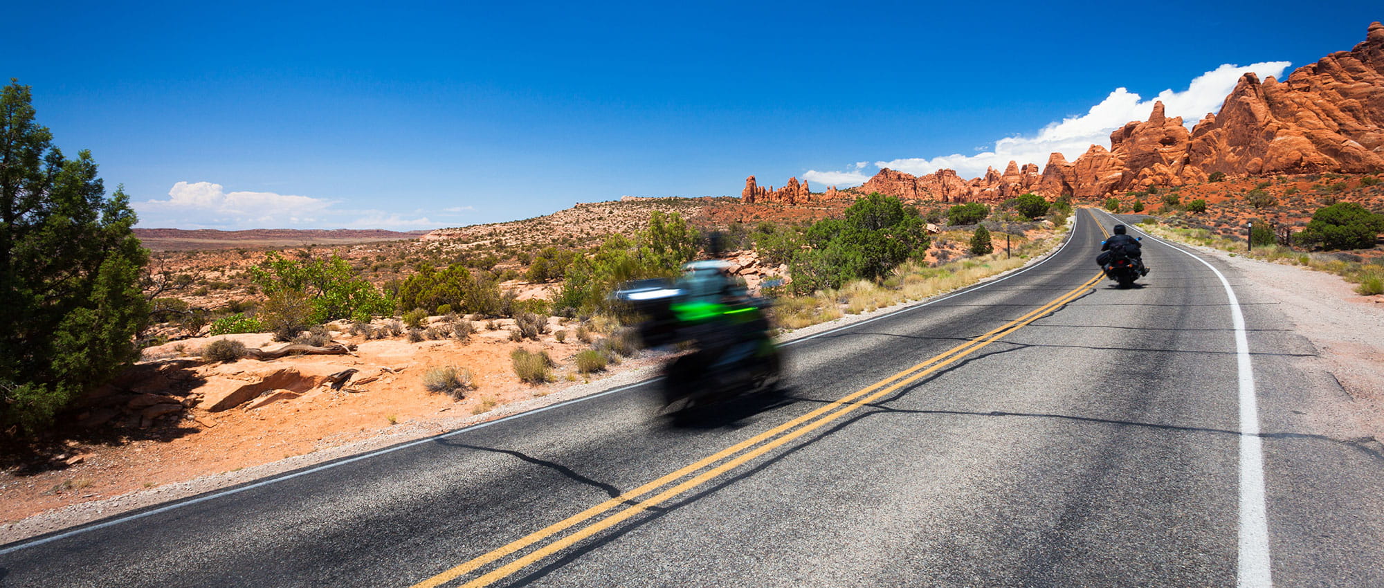 Two motorcyclists on a barren country road in the desert
