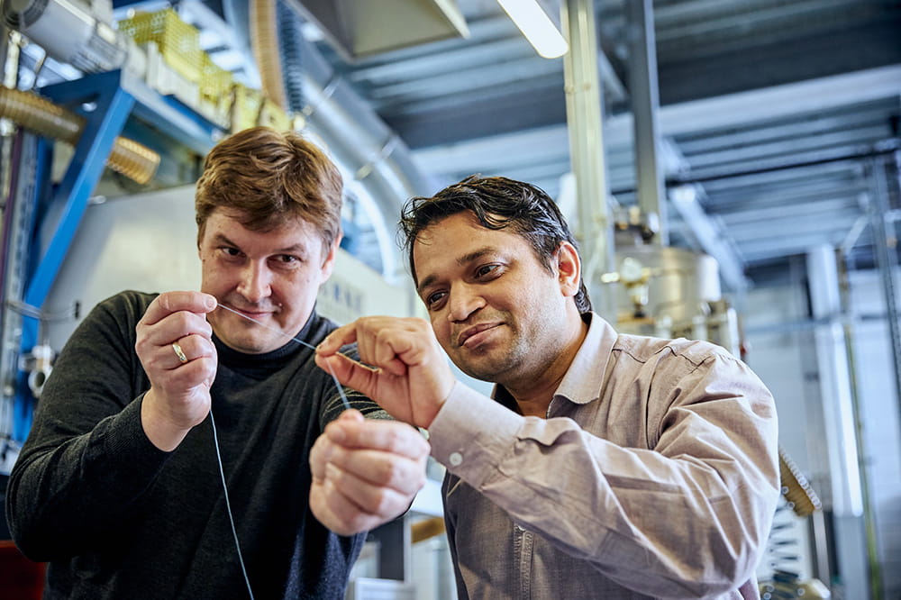 Two men in a factory holding a thin synthetic thread together