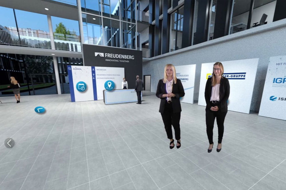 Sina Etter and Lena Winkenbach standing in a digital hall. In the Background are several companies listed on banners
