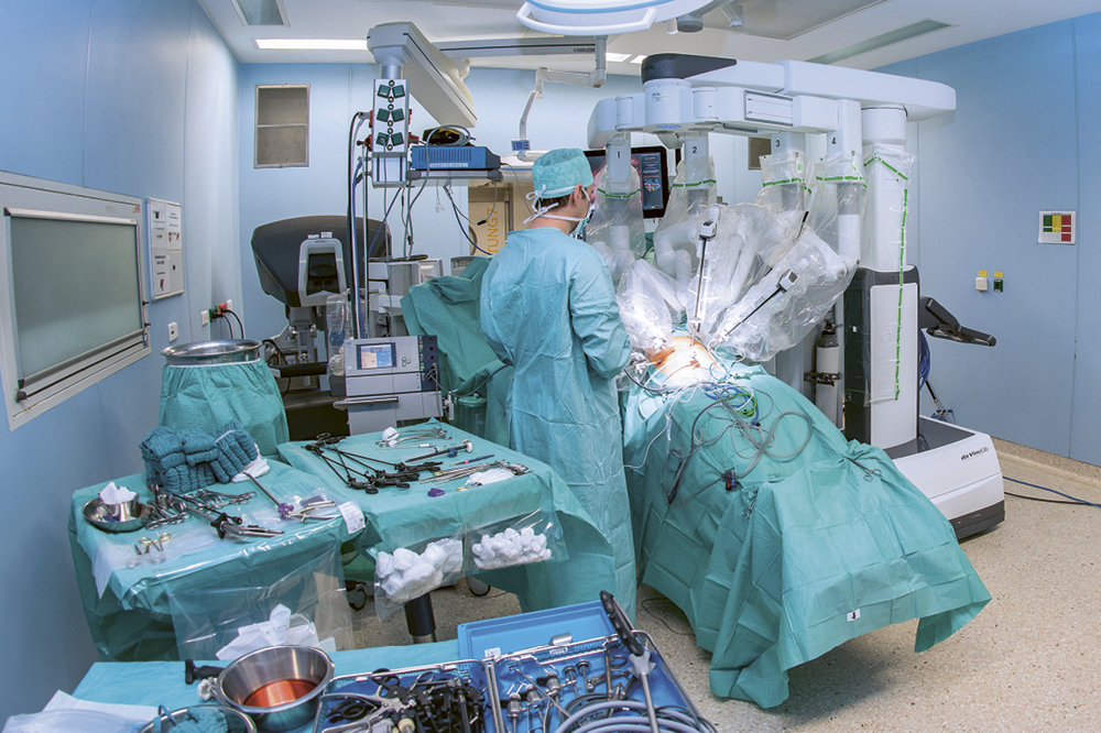Picture of an operating room in which a doctor and a robot are operating on a person. 