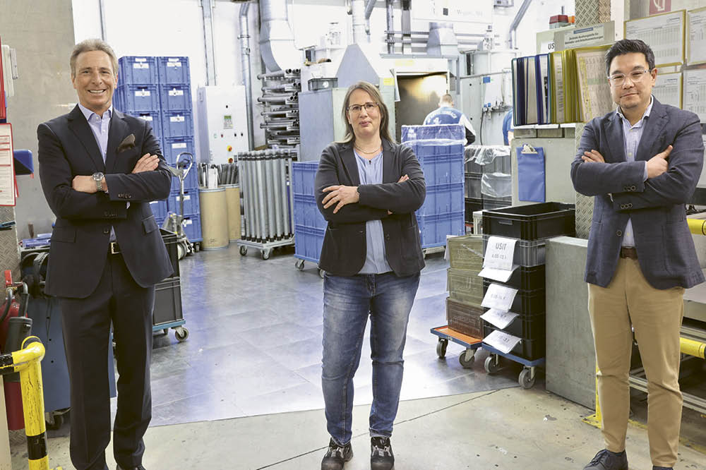 Ralf Schmid, Annette Reisner-Schaab and Dr. Clemens Elliger are standing in a row in the factory.