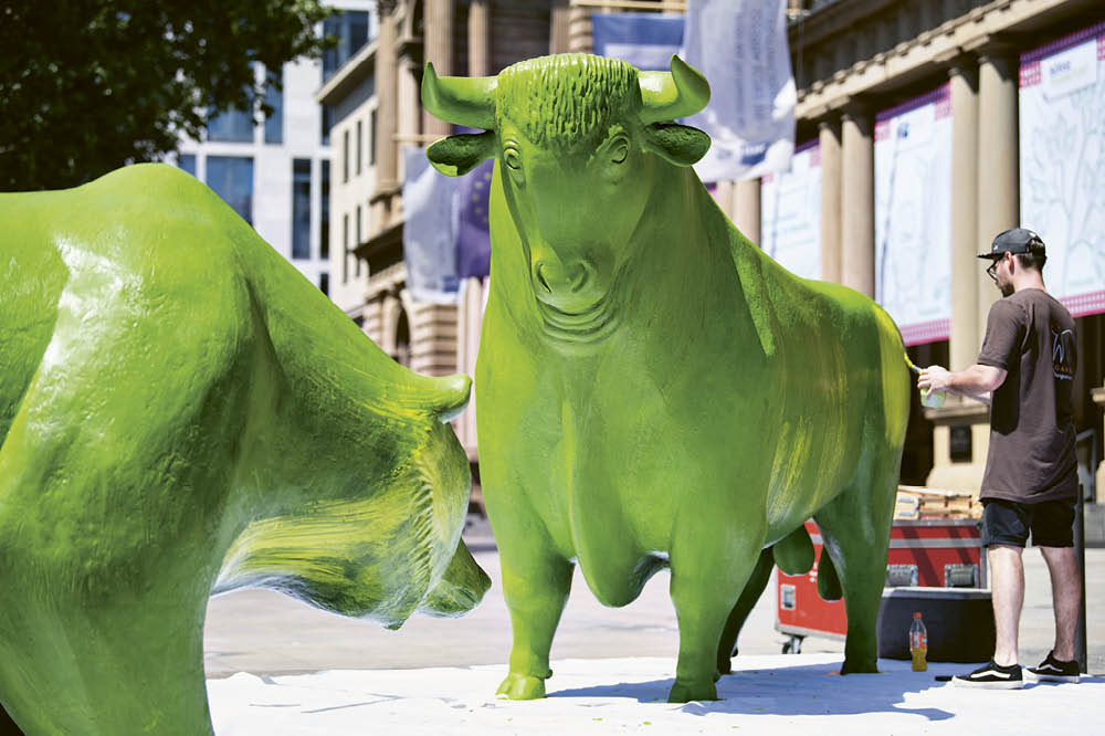 A man paints a bull statue with green paint.