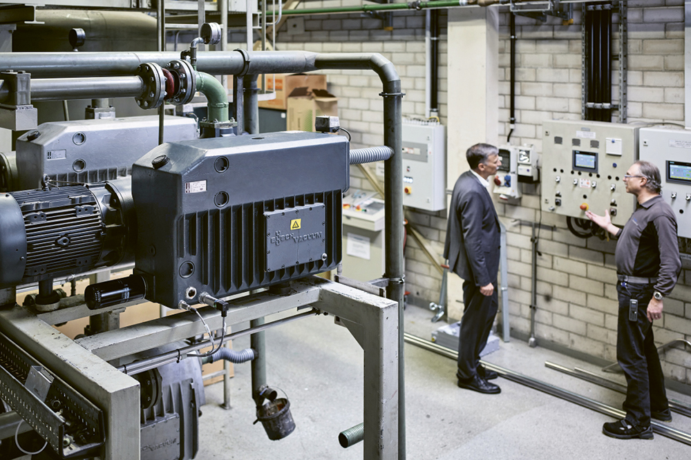 Two men are looking at compressors in a factory.