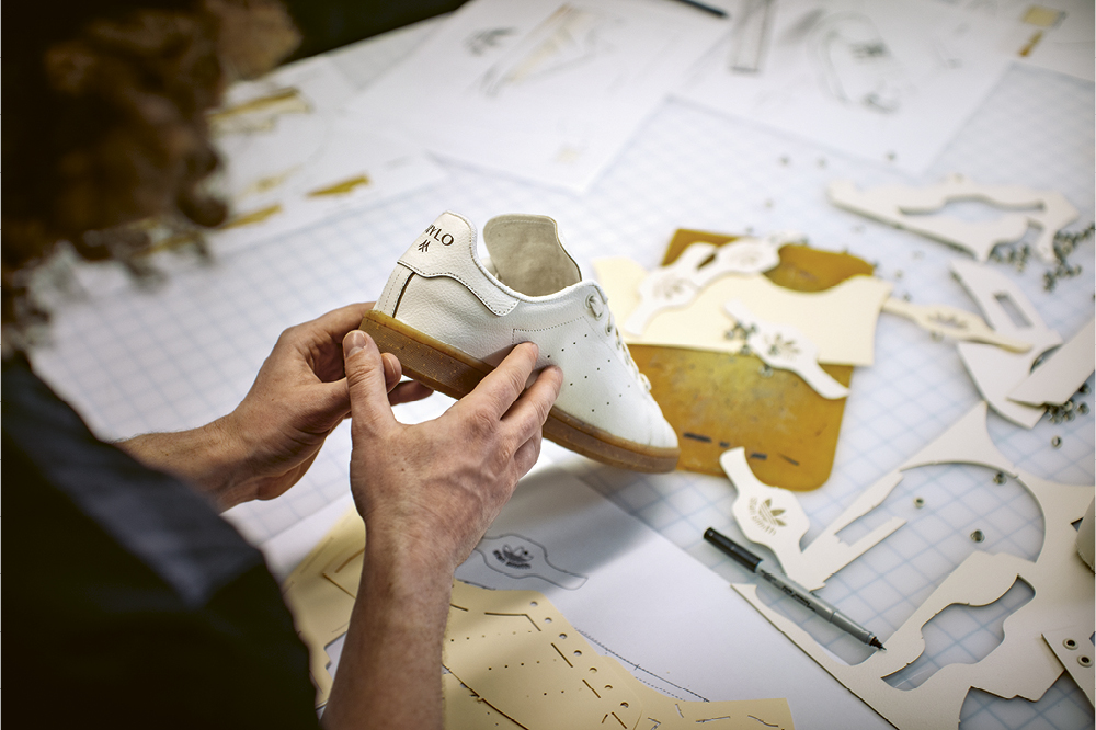 A man holds a shoe in his hand and in the background is lying the cut out pattern.