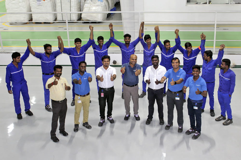 A group of people dressed in blue overalls are standing in two rows and throw their hands in the air. 