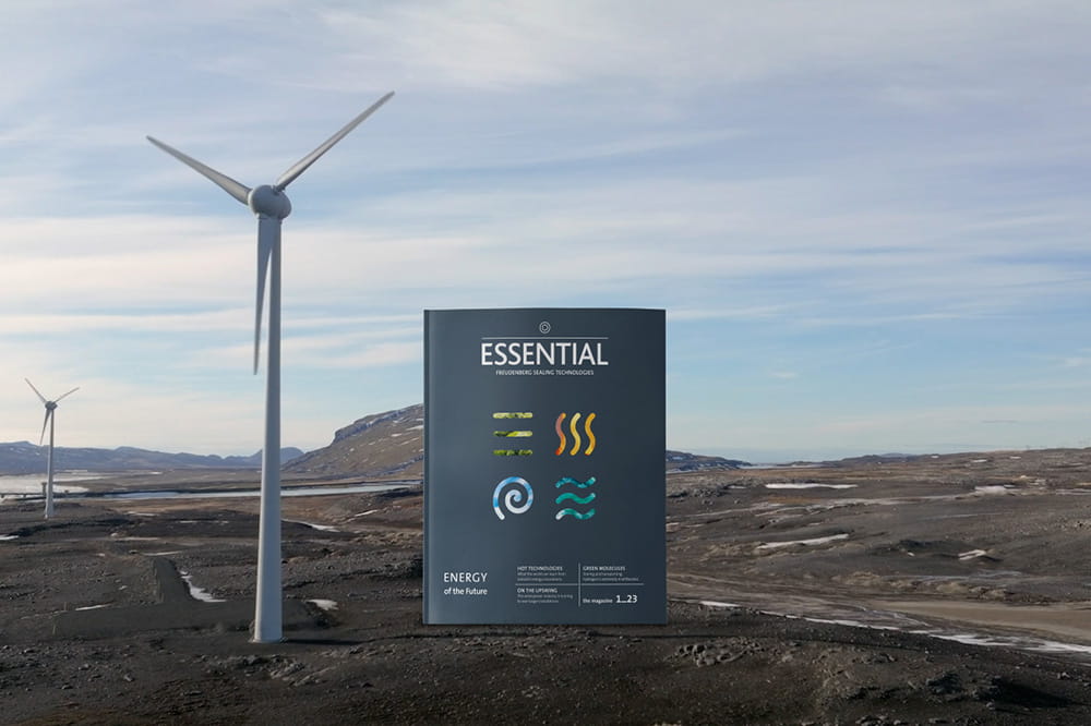 The ESSENTIAL magazine with the topic of renewable energies stands next to a wind turbine in the landscape.