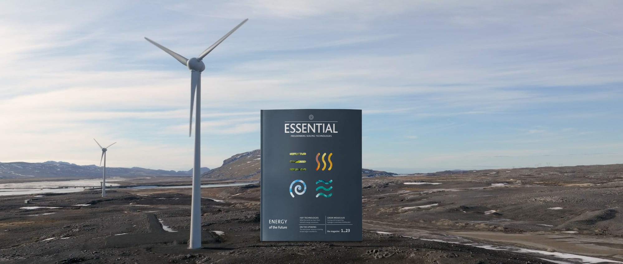 The ESSENTIAL magazine with the topic of renewable energies stands next to a wind turbine in the landscape.