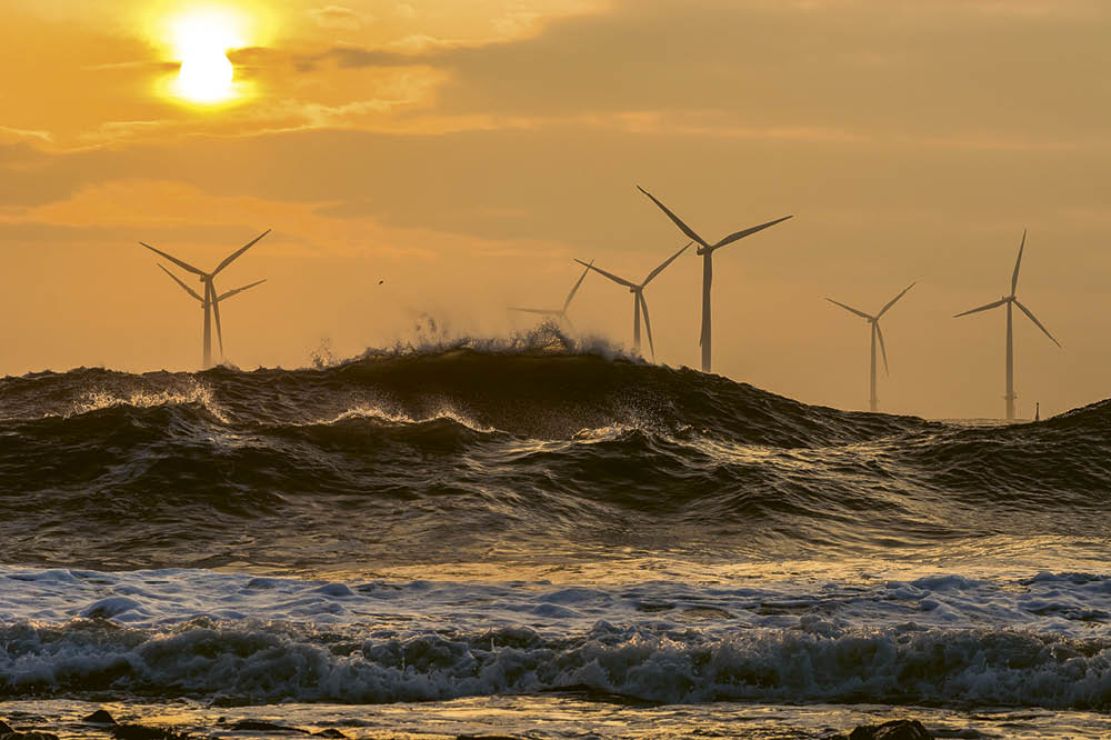 Sunset by the sea with windmills behind the waves.