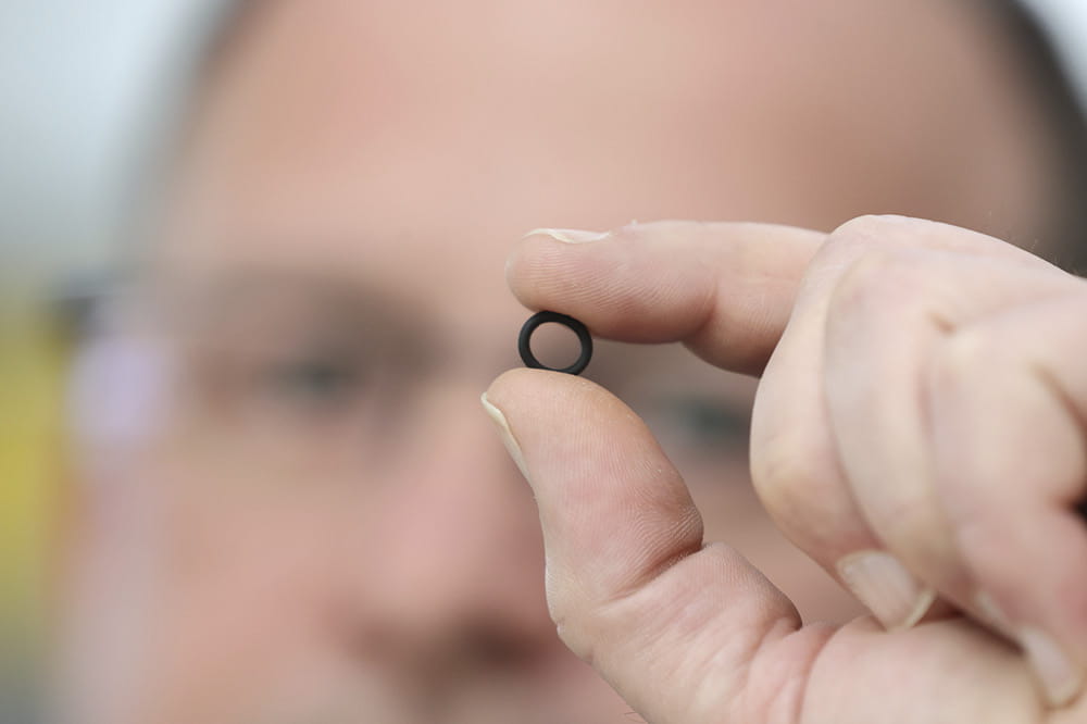 A man holds a sealing ring between his fingers in front of his face.