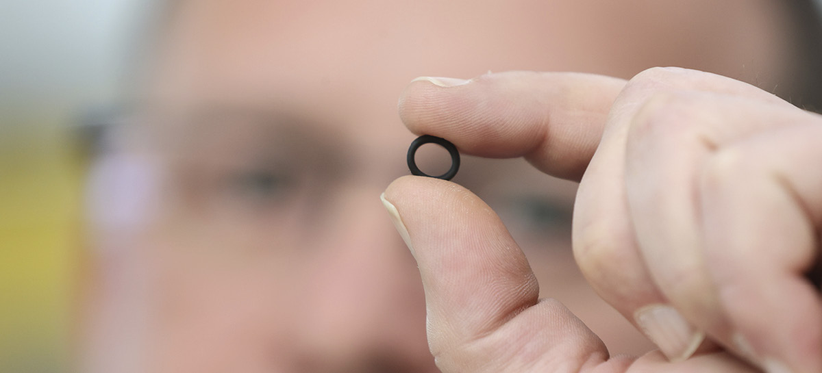 A man holds a sealing ring between his fingers in front of his face. 