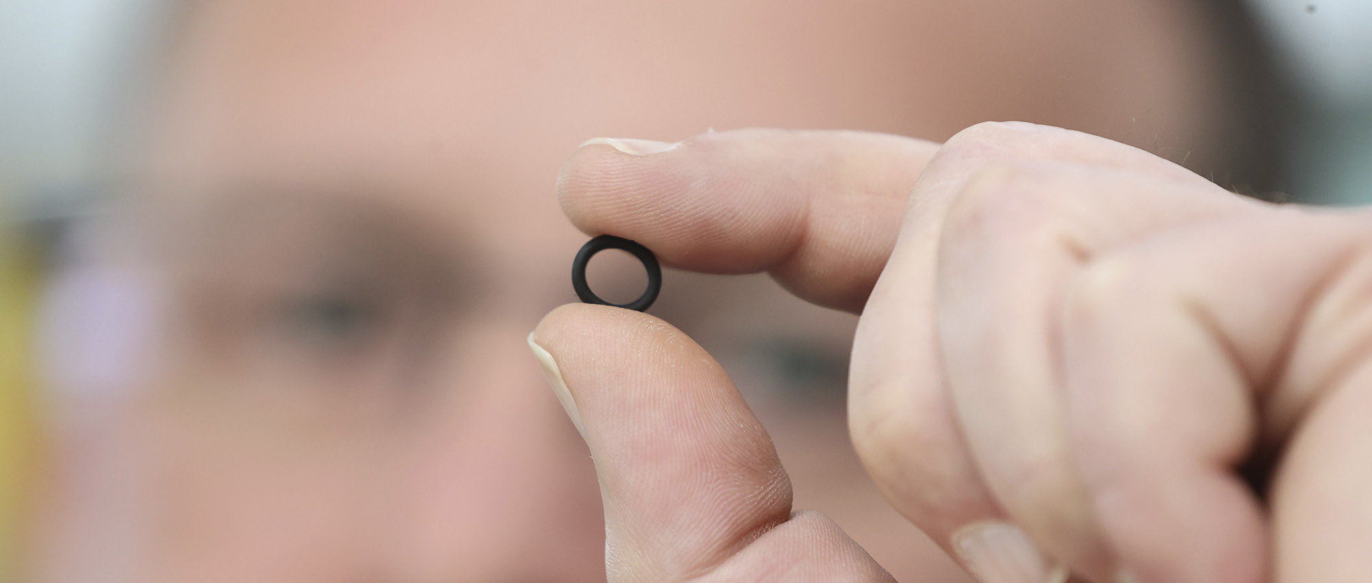 A man holds a sealing ring between his fingers in front of his face.