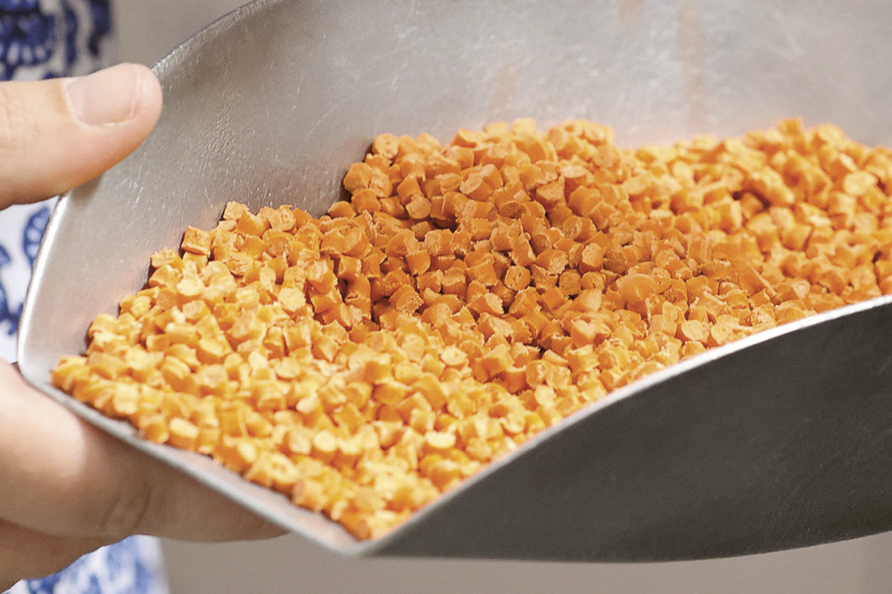 A scoop full of orange high-performance plastic Quantix® ULTRA.