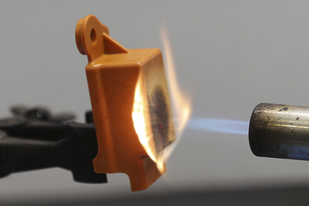 A flamethrower throws a flame onto an orange piece of plastic and burning but not melting it. 