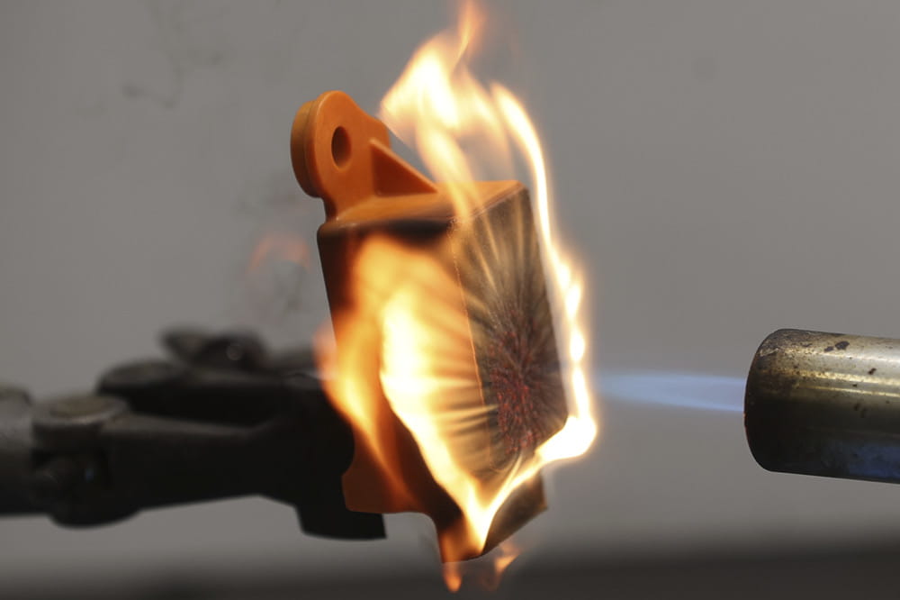 A flamethrower throws a big flame onto an orange piece of plastic and burning but not melting it.