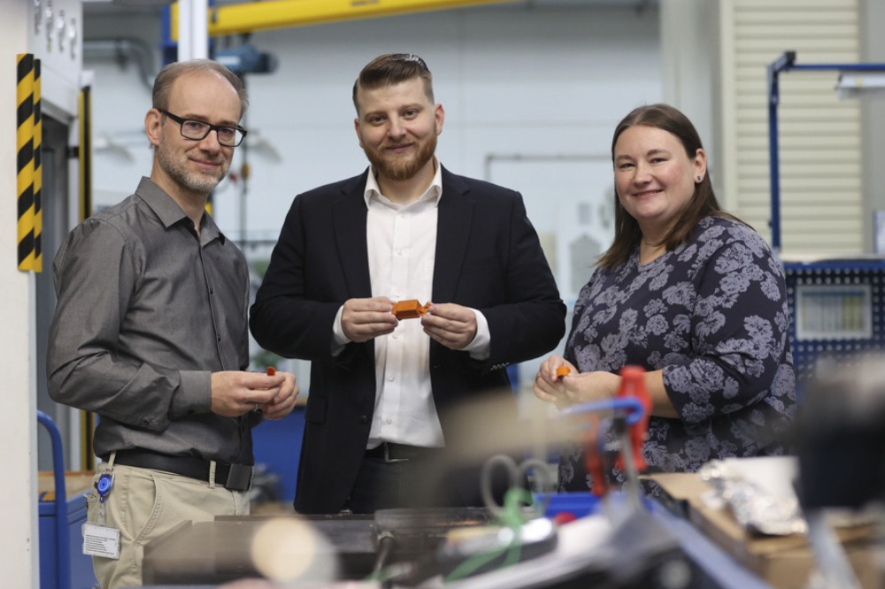 A woman and two men, Kira Truxius, Marco Sutter and Björn Hellbach, hold a piece of Quantix® ULTRA high-performance plastic in their hands and smile at the camera.