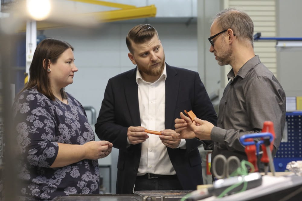 A woman and two men, Kira Truxius, Marco Sutter and Björn Hellbach, hold a piece of Quantix® ULTRA high-performance plastic in their hands and are immersed in a conversation.