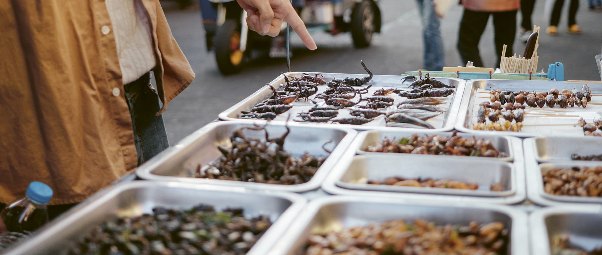 A man at a market points a finger at insects on display. Copyright: iStock/staticnak1983