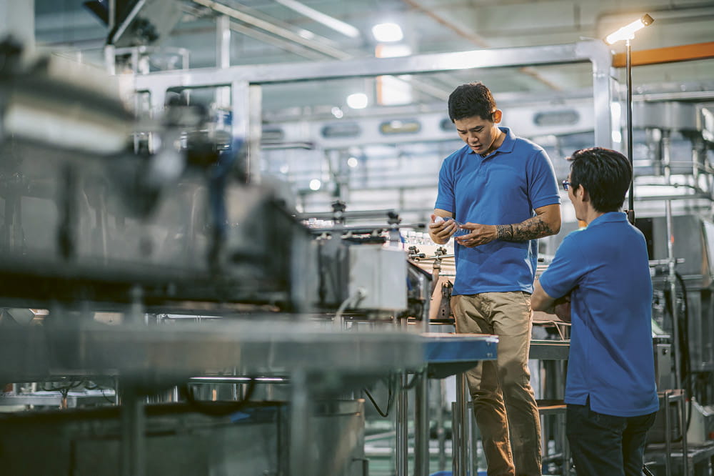 Two men in blue shirts are standing in a modern drinking water bottling plant.