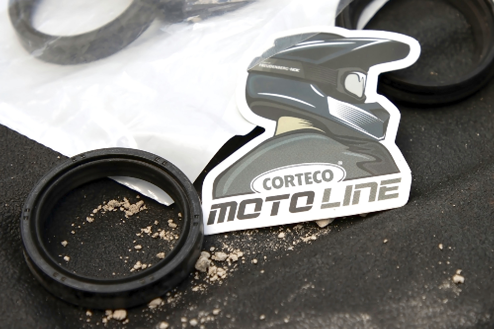 A sticker of a person with a motorcycle helmet on their head with the inscription Corteco Moto Line is lying on a table next to a seal. 