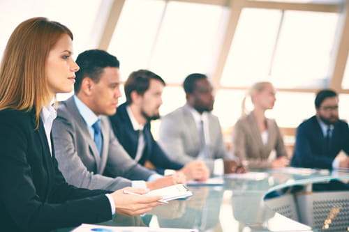 Six people in suit sitting at round glass table
