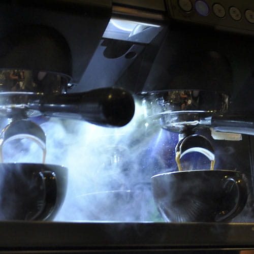 Close up of two freshly brewed espressos with steam rising from portafilter machine with lighting in background
