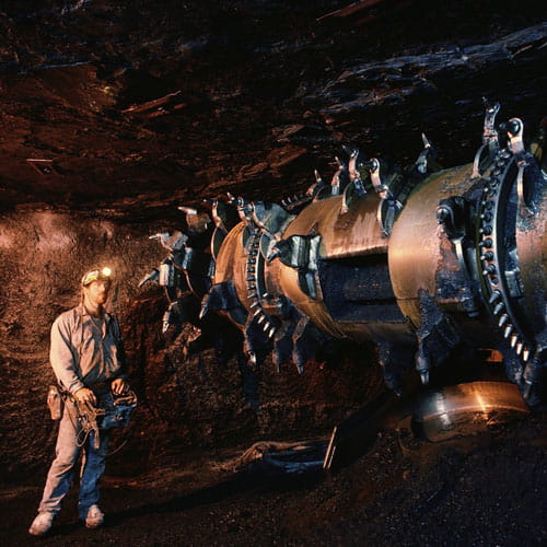 Construction worker stands in front of tunnel boring machine with protective equipment in underground environment 