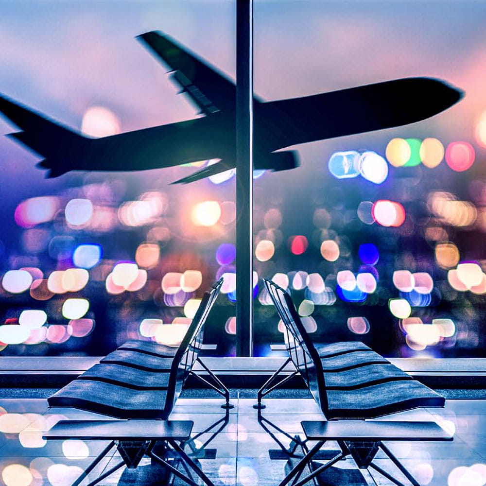 Airplane taking off in front of colorful lights in darkness with waiting area of an airport in foreground