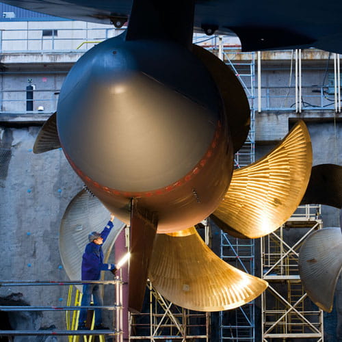 Close-up of a ship's propeller being lighted from the side and inspected by a technician