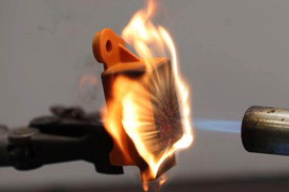 Heat testing experiment: A metal rod with a blue flame heats an object clamped in place, causing it to catch fire.