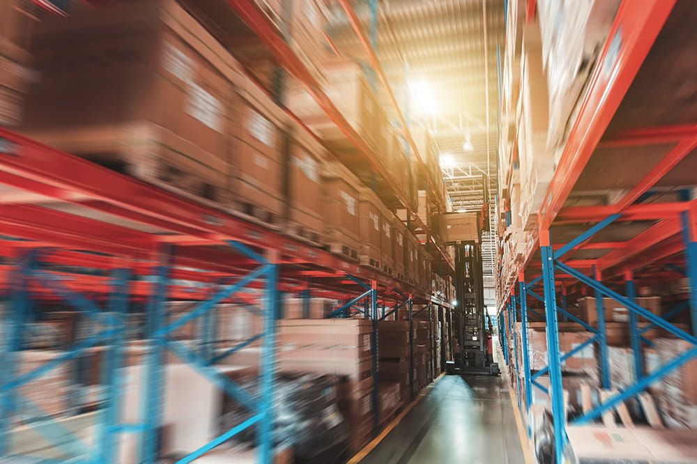 Forklift truck moves a package through a row of racks with stored boxes in a warehouse