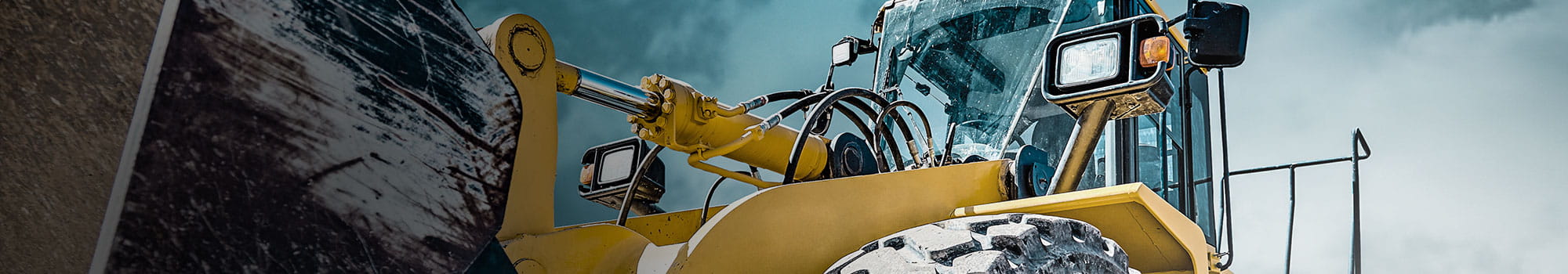 Yellow front loader construction machine in front of cloudy sky