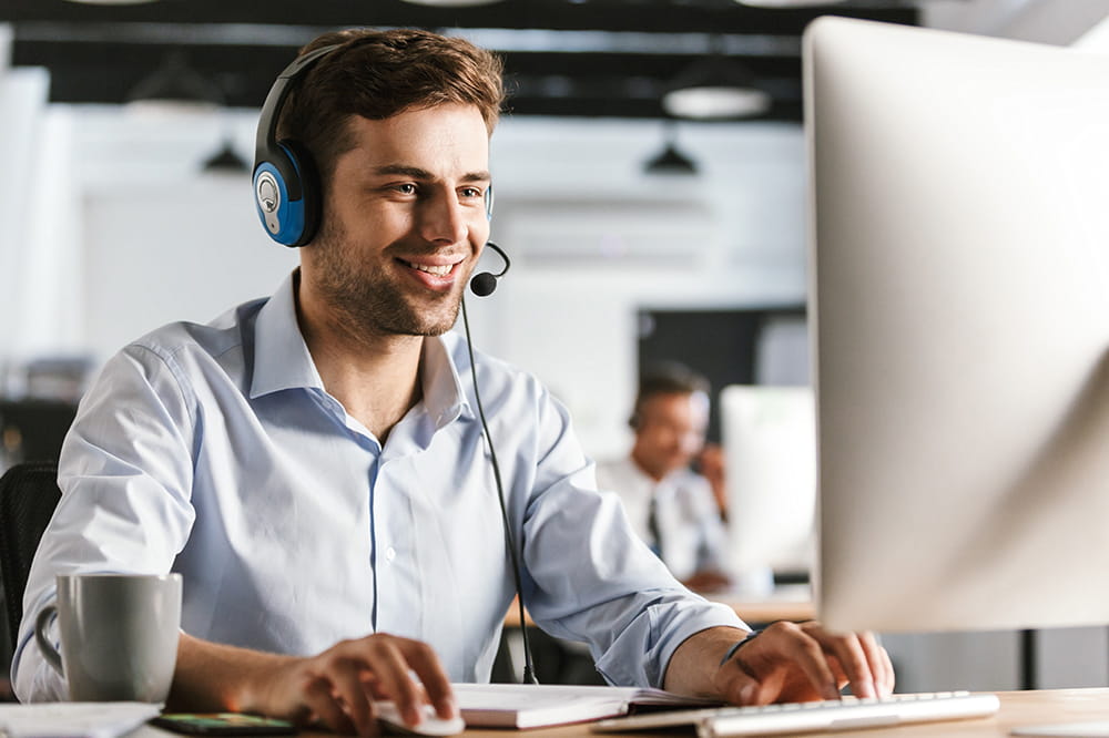 Call center employee with headset in front of a computer and another employee in the background