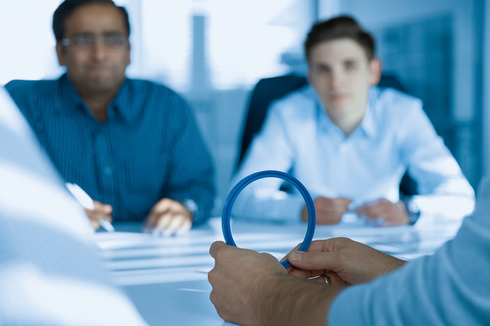 Two hands hold up a blue seal. Two men in blue shirts sit opposite each other