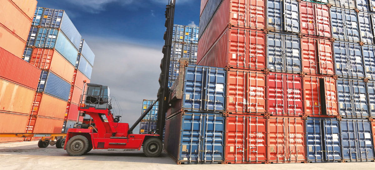 Forklift truck loads containers between other shipping containers