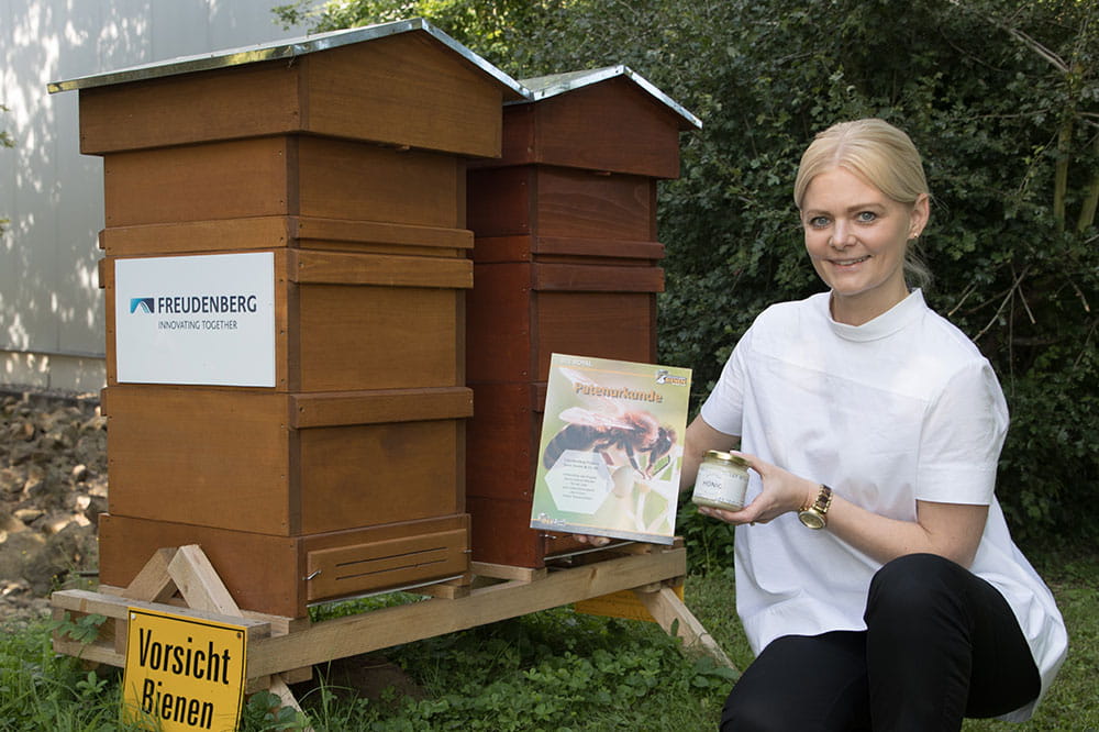 Sina Etter, Marketing Managerin Process Industry Deutschland, kniet vor den zwei Bienenstöcken und hält die Patenurkunde in die Kamera.
