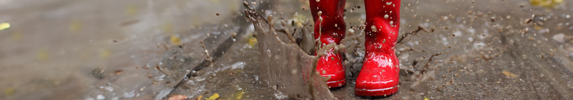 Kind in roten Gummistiefeln springt in eine Pfütze, Nahaufnahme