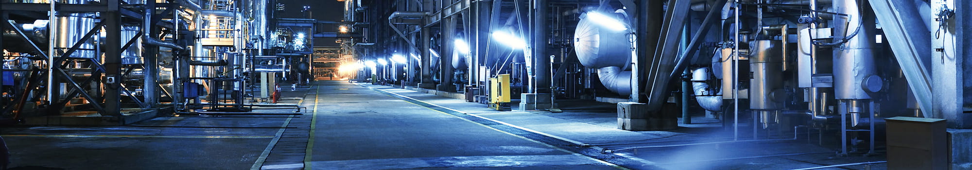 Chemiewerk bei Nacht mit mehreren Rohren in blauer Farbe.