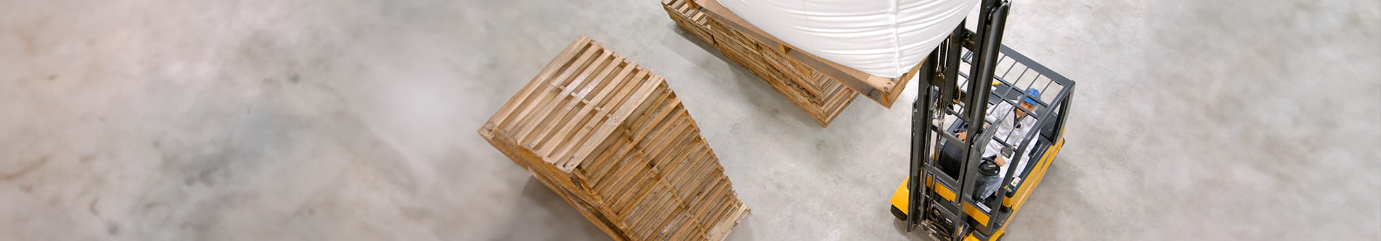 Gabelstabler transportiert einen großen Sack mit Materialen und daneben stehen Platten mit Holz