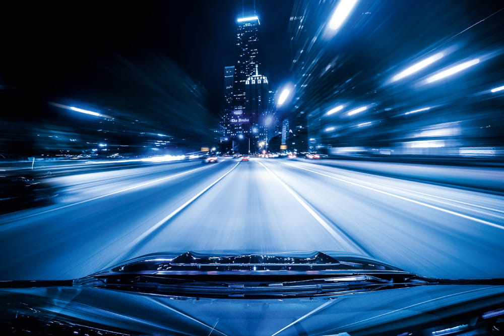 Ausblick aus Autorückscheibe: Beleuchtende Straße in einer Stadt bei Nacht