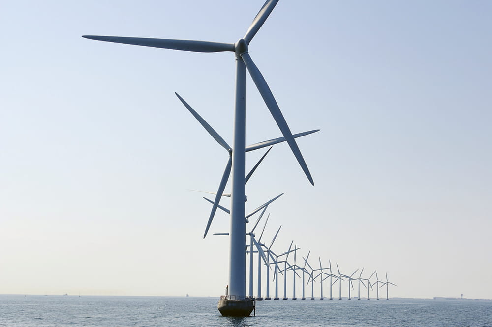 Eine Reihe von Windrädern die im Meer stehen.