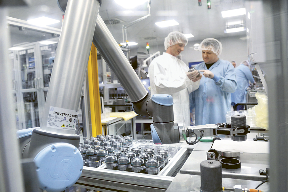Roboterarm im industriellen Einsatz, dahinter Mitarbeiter in Arbeitskleidung 