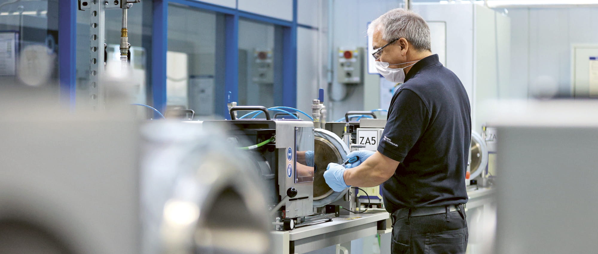 Mitarbeiter mit Maske arbeitet an industrieller Maschine.