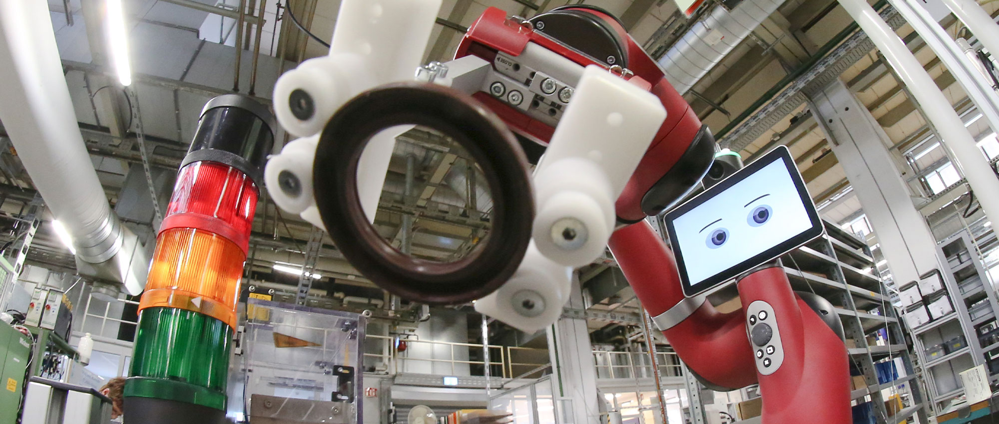 Ein Mann bedient den roten Roboter Cobot in einer Fabrik im Hintergrund