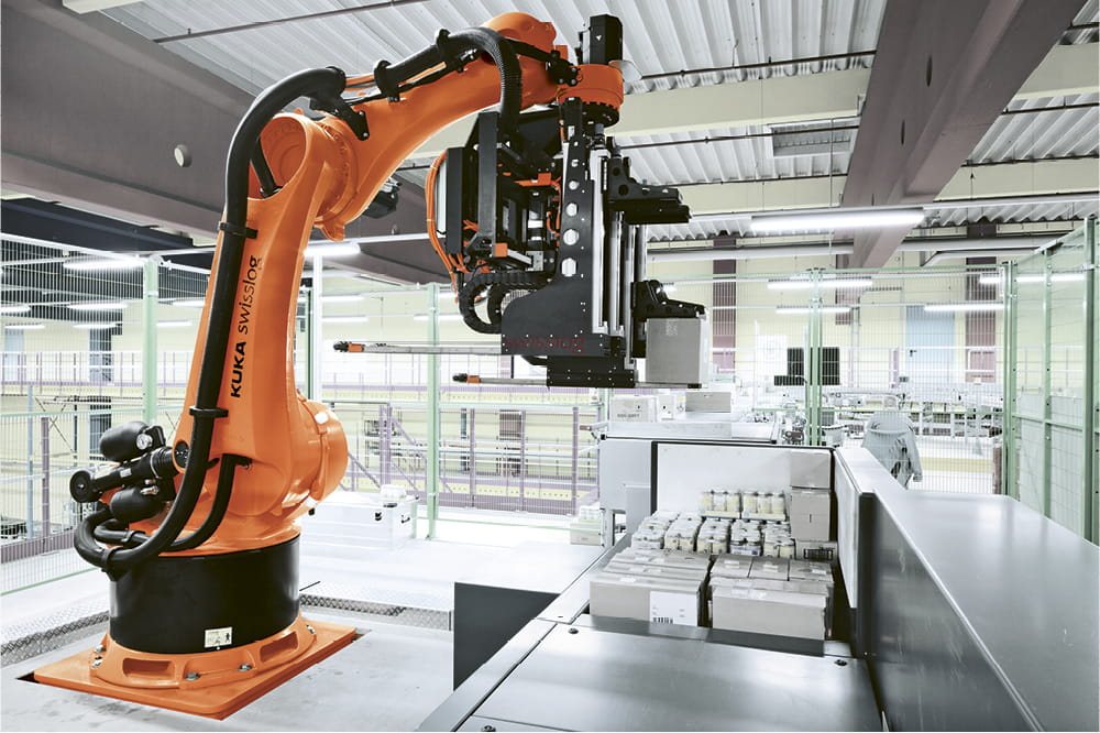 Orangener Roboterarm stapelt kleine Pakete in einer Fabrik