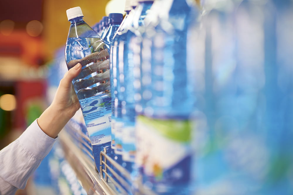 Eine Wasserflasche wird aus einem Regal gegriffen. Copyright iStock / mediaphotos